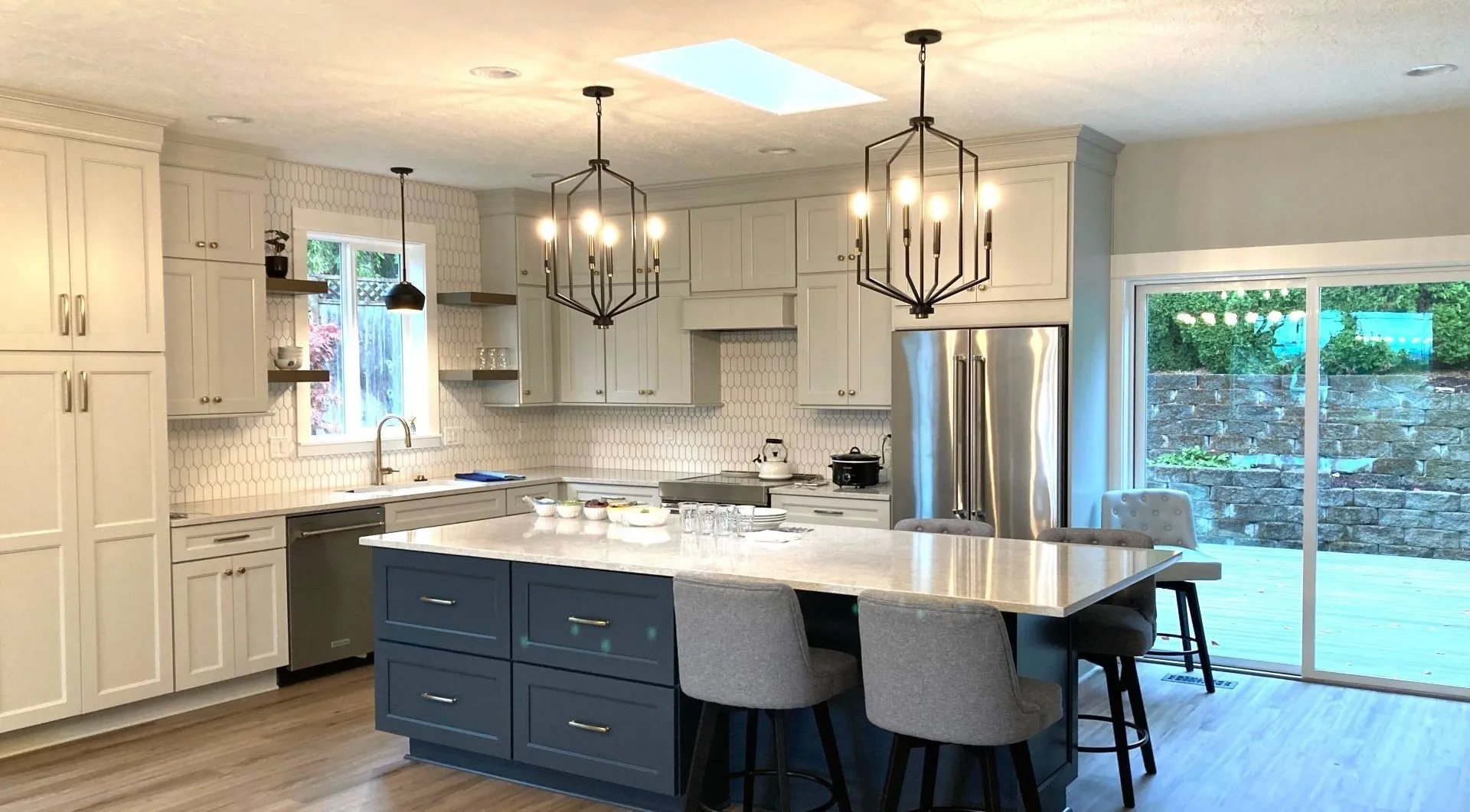 Custom kitchen remodel with large island seating, white cabinetry, hex tile backsplash, and pendant lighting.