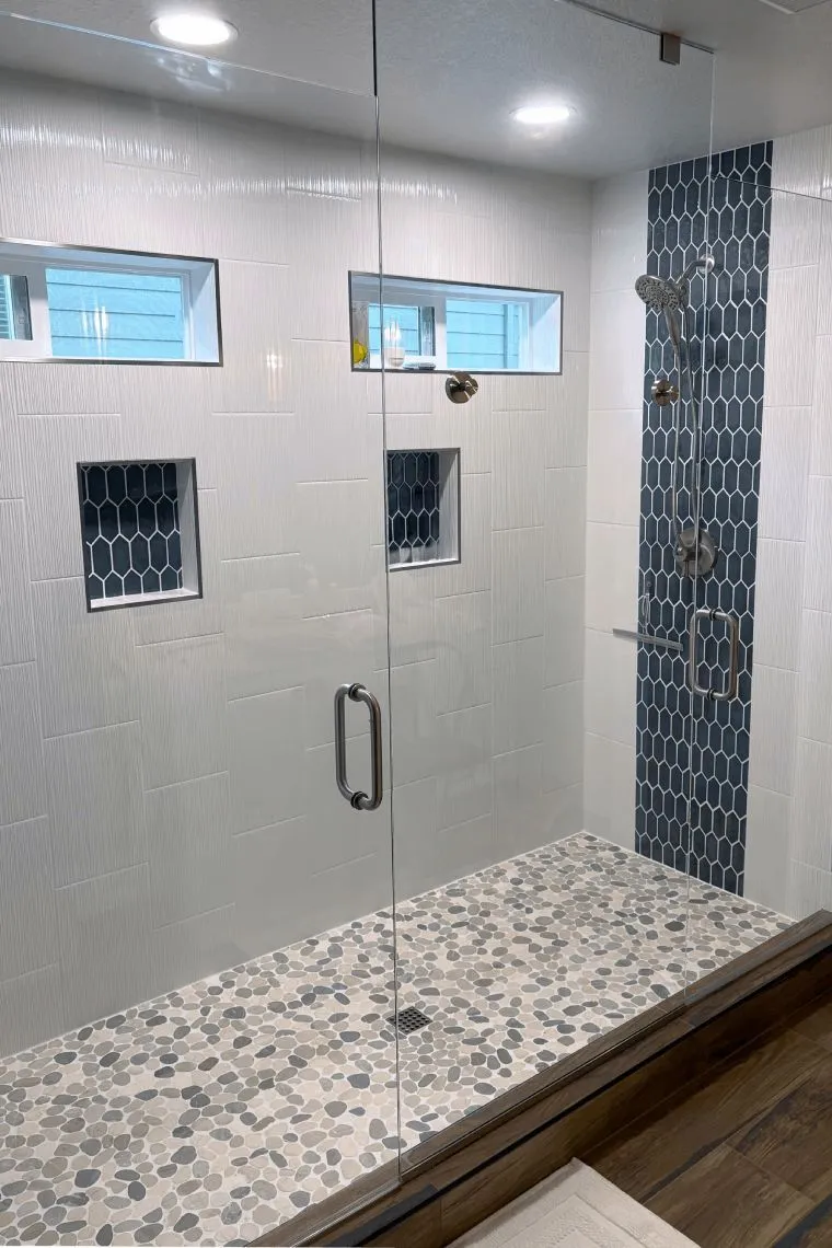 Bathroom remodel with two-person walk-in shower, glass enclosure, and navy tile accent in southeast Portland home