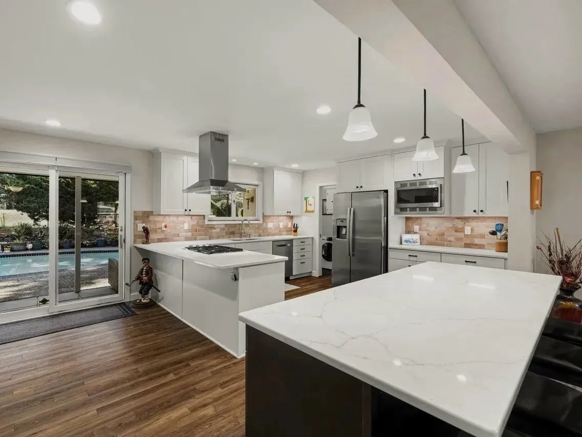Wide view of the remodeled kitchen showing the island, peninsula, structural opening, and backyard access