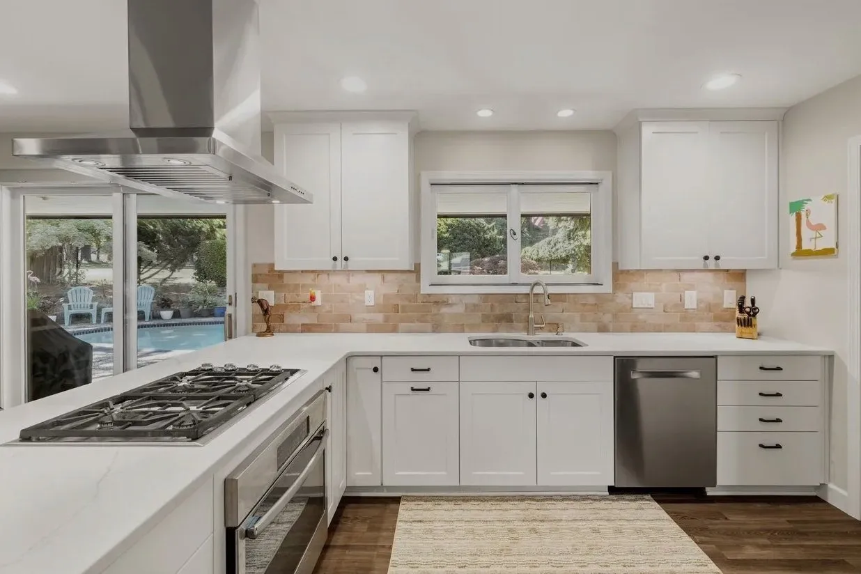 Remodeled kitchen work area with white cabinetry, cooktop, sink, dishwasher, countertops, and stainless steel range hood