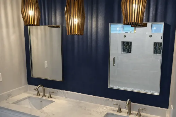 Modern bathroom remodel with double vanity, blue accent wall, pendant lighting, and large mirrors in a Portland home