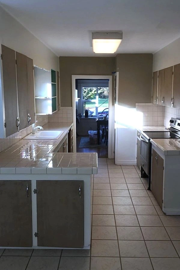 Original narrow galley kitchen before renovation in a Portland home in the Brooklyn neighborhood, showing dated cabinets, tile countertops, and limited workspace.